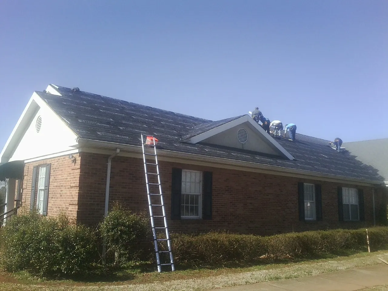 Crew tearing shingles off a brick ranch roof with a ladder set — Emergency Roof Repair work by our crew in Gowrie