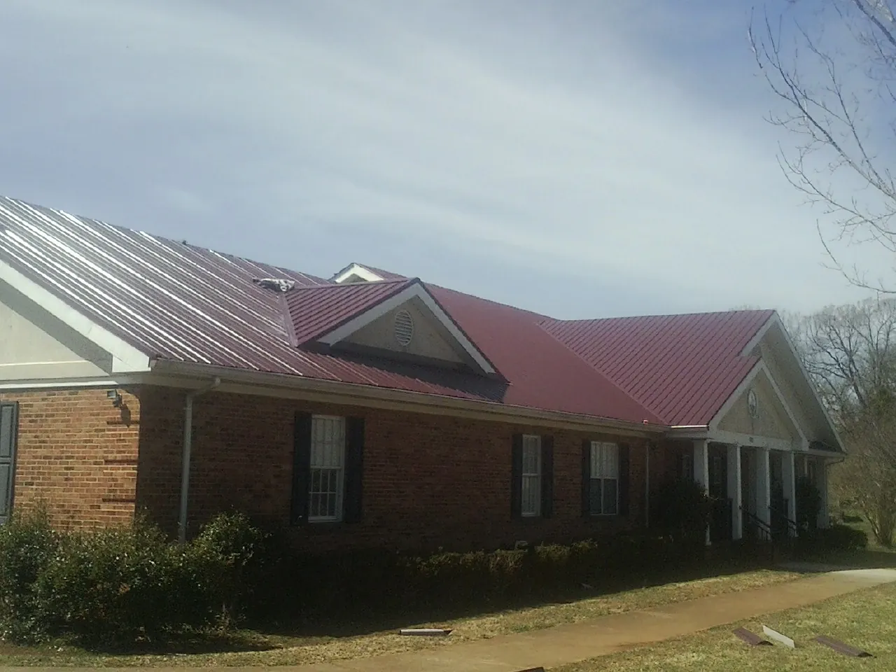 Red metal roof with gabled entries on a long brick building, from a Hail Damage Roof Repair job in Gowrie