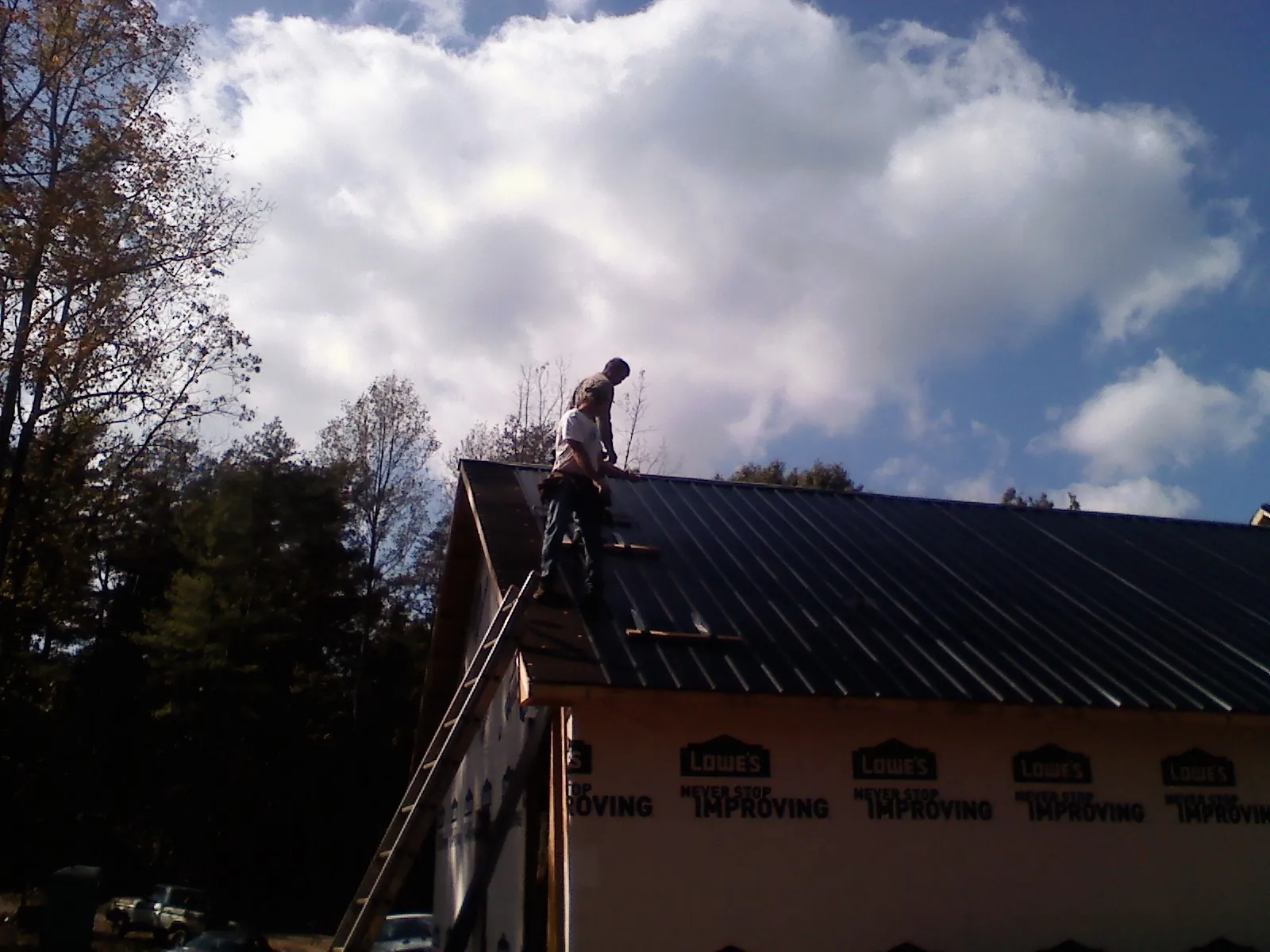 Roofer fastening dark metal panels high against a cloudy sky, from a Roof Inspection job in Gowrie