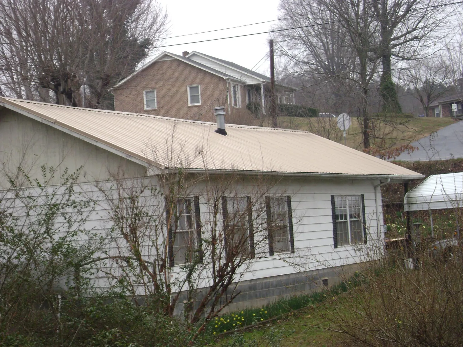 Tan metal roof on a white sided house set into a hillside — Commercial Roofing by Roofing Brothers in Gowrie